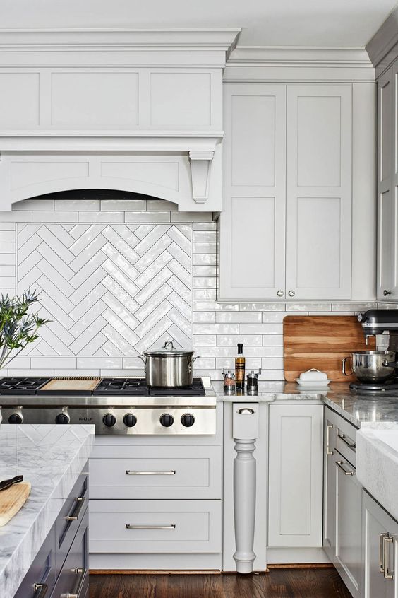 A white vintage farmhouse kitchen with shaker cabinets, a herringbone tile backsplash, and a dark kitchen island
