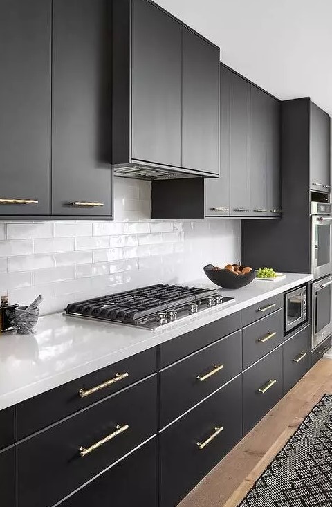 A chic black and white kitchen with sleek matte black cabinets, white countertops, white thin tiles on the backsplash and gold fixtures