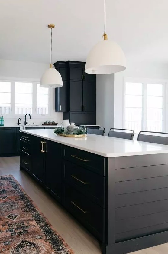 a contrasting kitchen with black planked cabinets and a kitchen island, white countertops and white pendant lamps