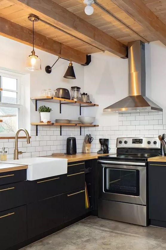 A black and white farmhouse kitchen with matte cabinets, butcher block countertops, wooden shelves and ceiling, and a shiny metal hood