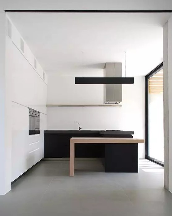 a minimalist black and white kitchen with white storage and upper cabinets, black lower cabinets and a kitchen island with a light stained table