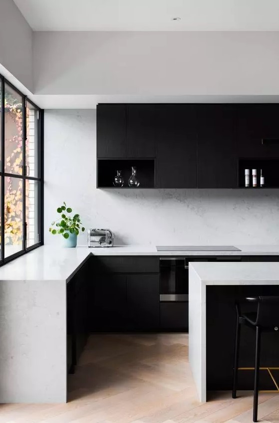 A minimalist black and white kitchen with matte black cabinets, white stone countertops and backsplash, and black stools is a chic place to hang out