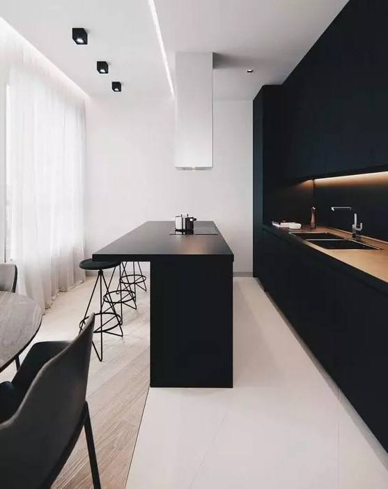 A minimalist black kitchen with built-in lights, a matte kitchen island, and a white range hood is a stylish and chic idea to rock