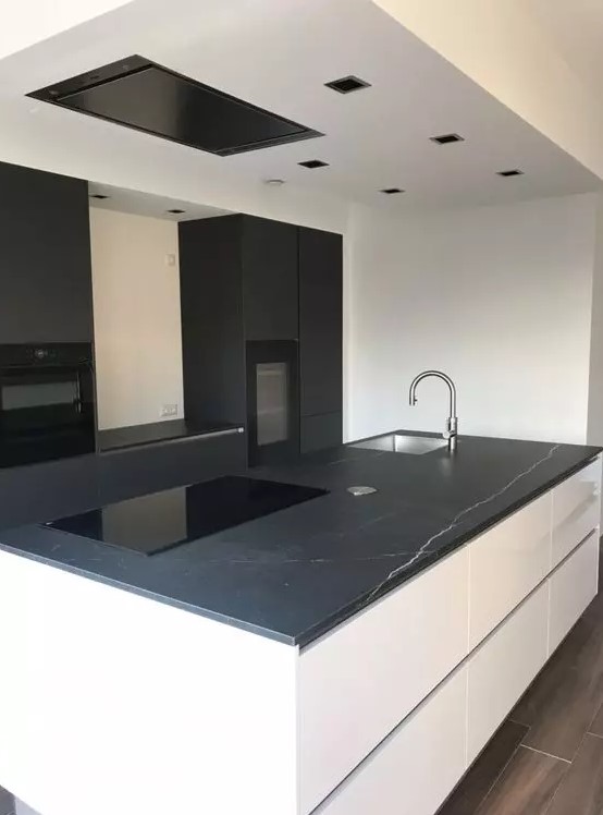 a minimalist kitchen with matte black cabinets, a large white island, black marble countertops and built-in appliances
