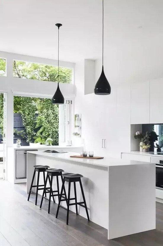 A minimalist white kitchen with several black accents such as a splashback and pendant lights, stools and fixtures feels airy and bright
