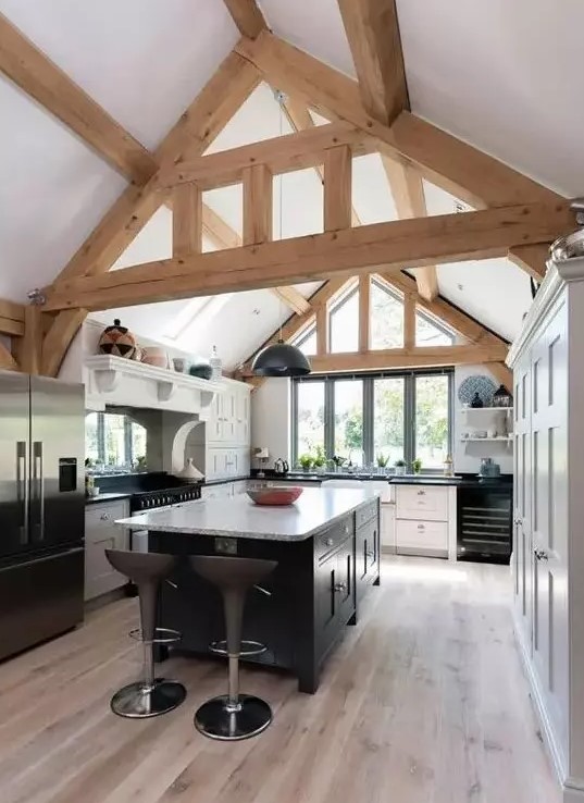 A modern barn kitchen with exposed beams, white cabinets and a black island and black appliances looks cool and fresh