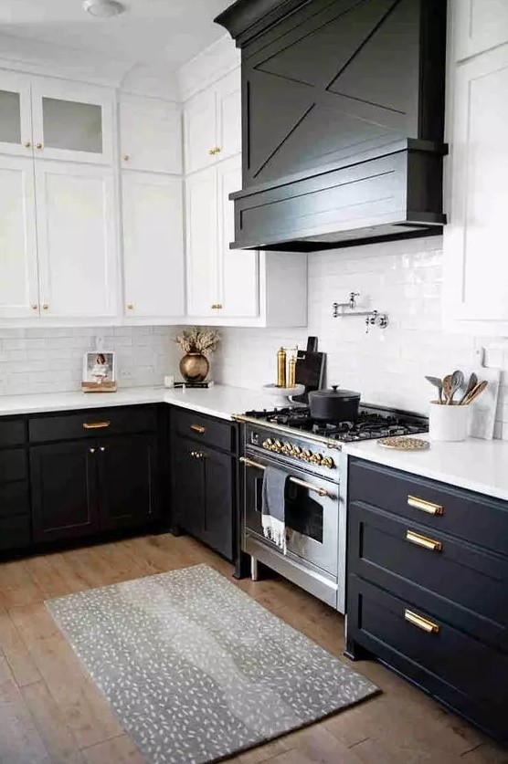 a modern farmhouse kitchen with black base cabinets and white upper cabinets, a large wood covered extractor hood and gold fittings