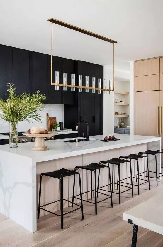 a sophisticated, modern kitchen with matte black cabinets, a white kitchen island with a white stone countertop, a chic chandelier and black fixtures