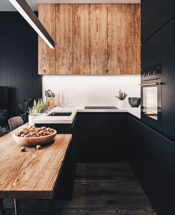 A chic black kitchen with a wooden table and a large extractor hood and white countertops looks very stylish and daring