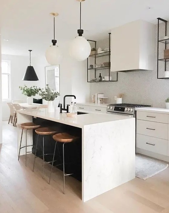 a chic, modern kitchen with sleek white cabinets, a white tile backsplash, a black kitchen island with a white stone countertop and pendant lamps