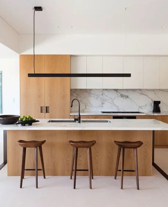 a chic modern kitchen with white and light stained cabinets, a large kitchen island with a white stone countertop and backsplash, a black pendant lamp