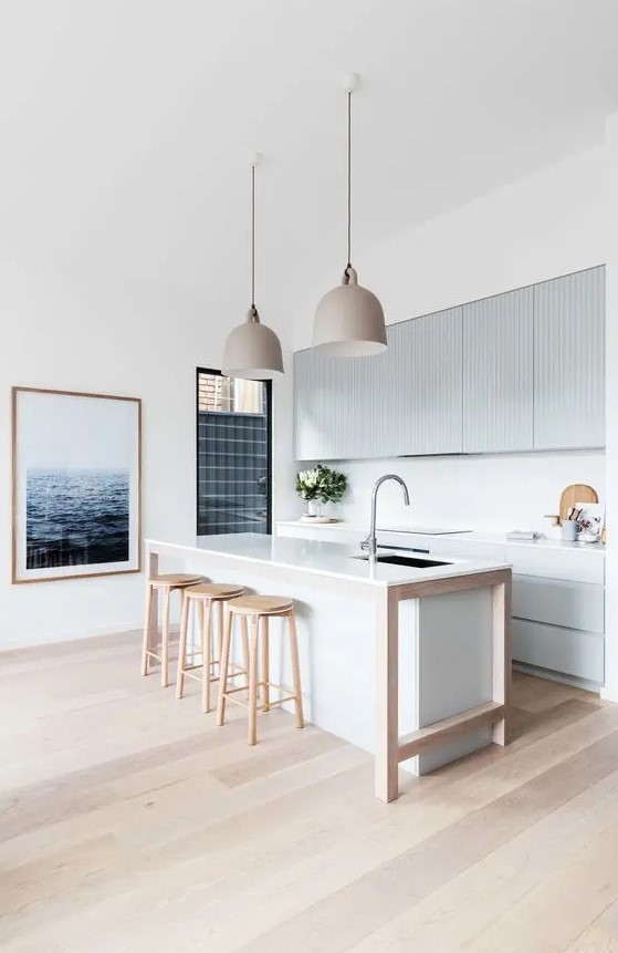 a modern beach kitchen with light blue ribbed cabinets and a white kitchen island, wooden stools and pretty pendant lamps