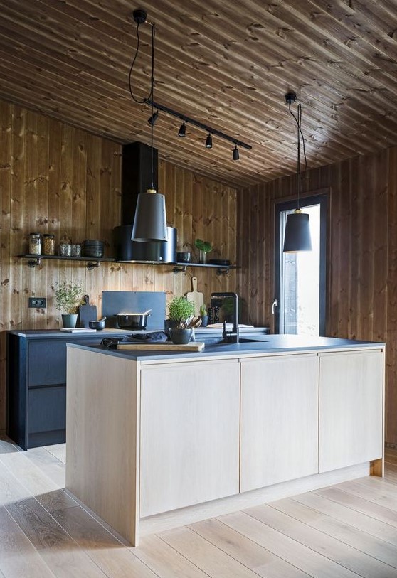A modern chalet kitchen, entirely clad in wood, with black metal cupboards and a plywood kitchen island, black worktops and a black extractor hood