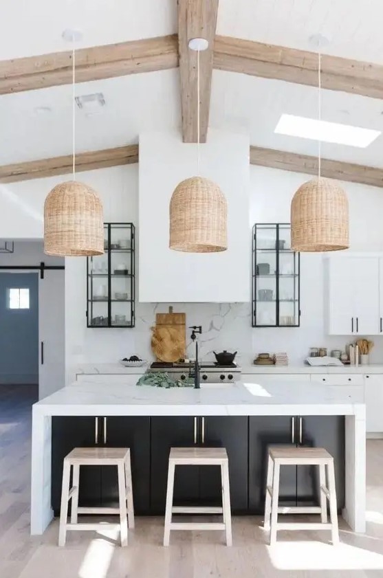 a modern white kitchen with black knob cabinets, a large range hood, a black kitchen island with a white countertop and woven pendant lamps