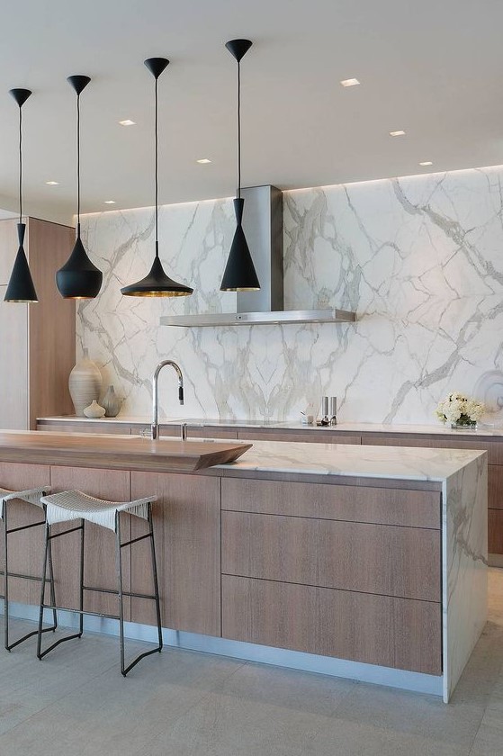 a modern kitchen with light stained cabinets and white marble countertops, a marble backsplash and a large kitchen island with plenty of drawers for storage