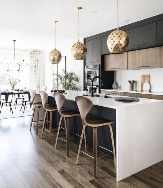 a modern kitchen with stained and black cabinets, a black island, white countertops and backsplash, and gold scale pendant lamps