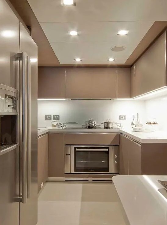 a modern taupe kitchen with sleek cabinets, white stone countertops and backsplash, built-in lights and neutral appliances