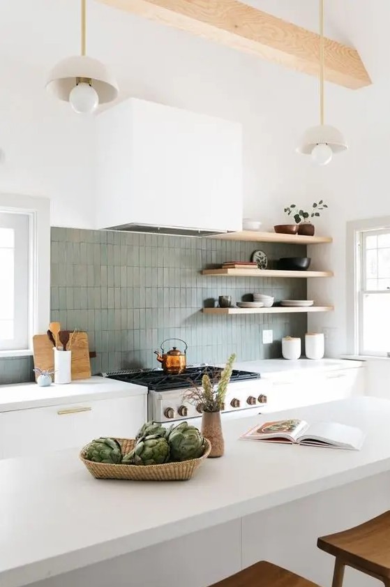 A modern white kitchen with elegant cabinets with gold handles, a gray thin tile backsplash, open shelving and a large kitchen island