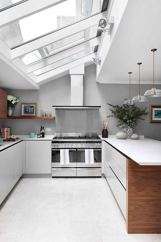 a large, neutral attic kitchen with a glazed ceiling, elegant white cabinets and countertops, pendant lamps and gray walls
