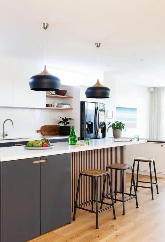 A beautiful modern kitchen with graphite gray and white cabinets, a white chevron tile backsplash, and striking black pendant lamps