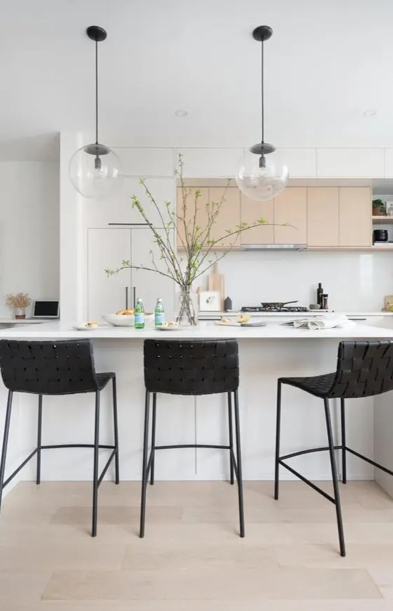 a beautiful modern kitchen with white and stained cabinets, a white kitchen island, black woven stools and pendant lamps