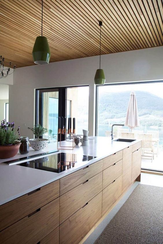 A pretty, modern kitchen with a brightly stained kitchen island, a wooden ceiling and green pendant lamps