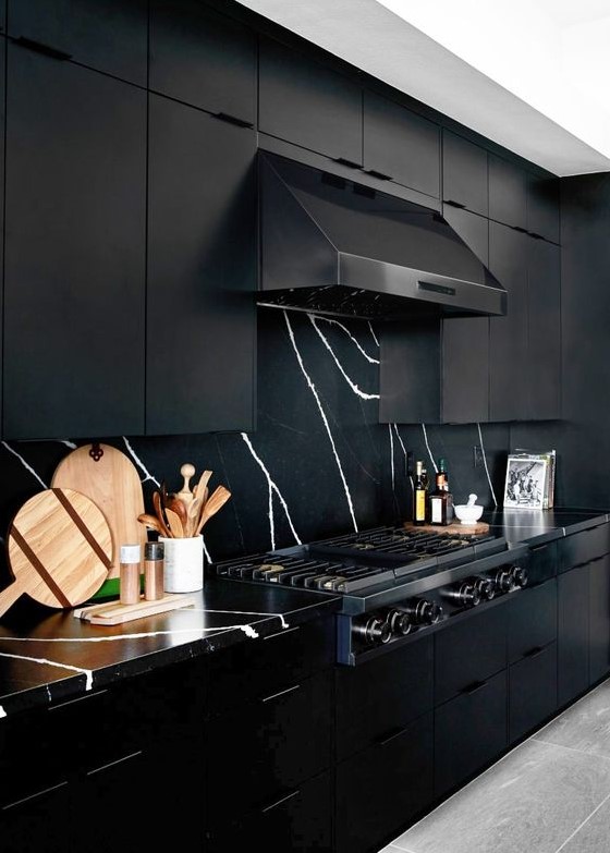 a sophisticated black kitchen with metal cabinets, a marble backsplash and countertops, and a black extractor hood