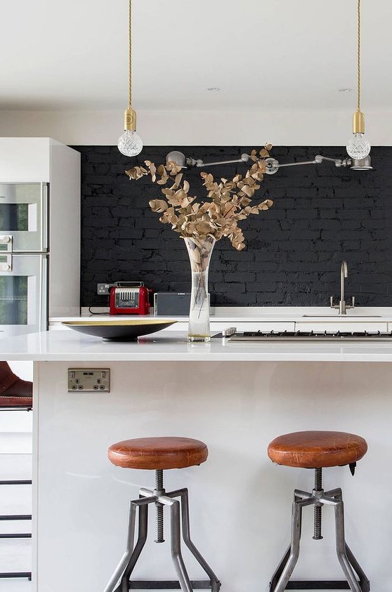 A stylish modern kitchen in white with a black brick backsplash, hanging light bulbs and gold accents is chic and bold