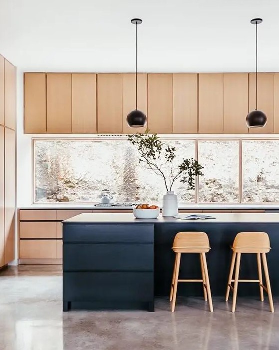 A stylish, brightly stained kitchen with a large window backsplash, a navy kitchen island, black pendant lamps and tall stained stools is perfection