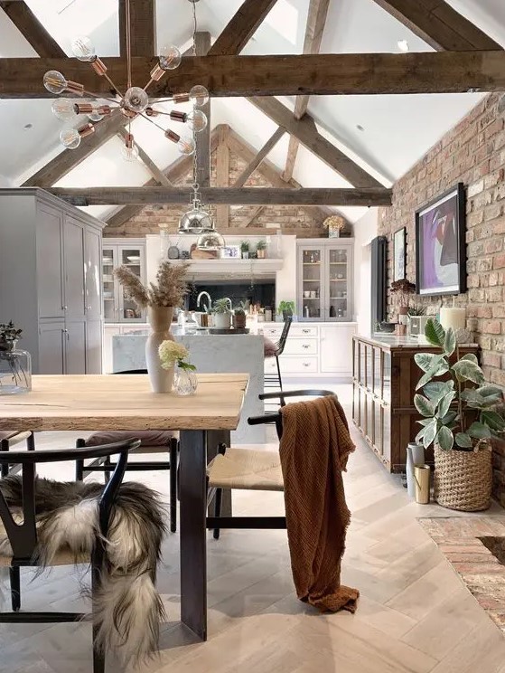 a barn kitchen with white cabinets, exposed beams, a white island, metal pendant lamps and artwork