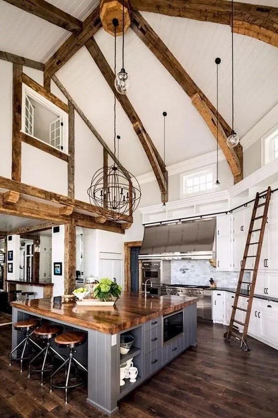 a barn kitchen with exposed beams, white shaker-style cabinets, and a gray-planked kitchen island that doubles as a table