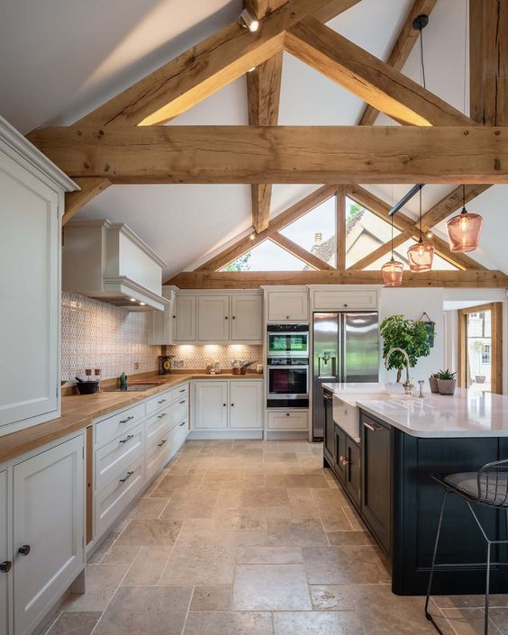 a chic barn kitchen with white shaker-style cabinets, a black island, exposed beams, and pendant lamps