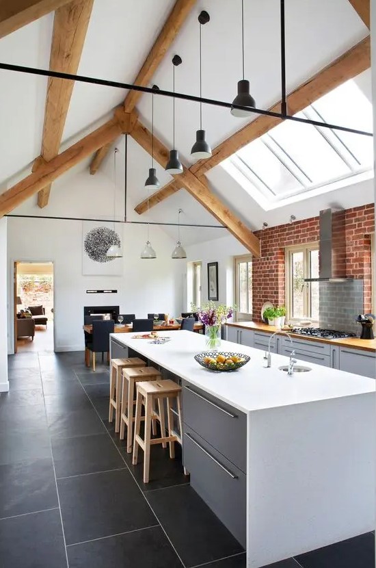 a modern barn kitchen with skylights, simple dove gray cabinets, butcher block countertops, exposed beams and black pendant lamps