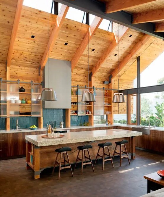 a modern barn kitchen with skylights, exposed beams, stained cabinets and an island, sliding door cabinets and metal lamps