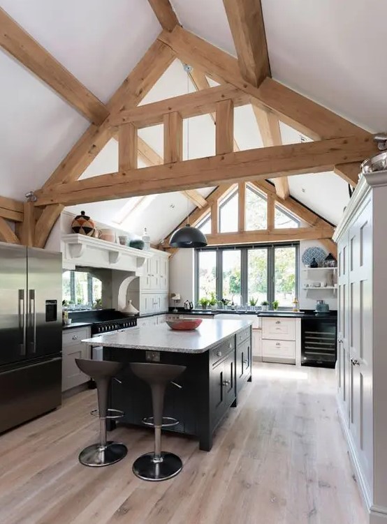 A modern barn kitchen with exposed beams, white cabinets and a black island and black appliances looks cool and fresh
