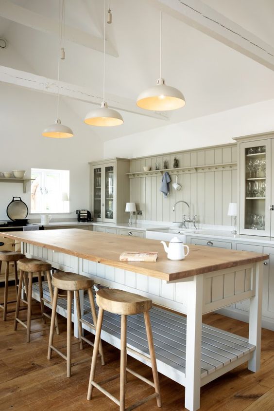 a neutral barn kitchen with bright green planked cabinets, a large planked kitchen island with butcher block countertop, wooden stools and pendant lamps
