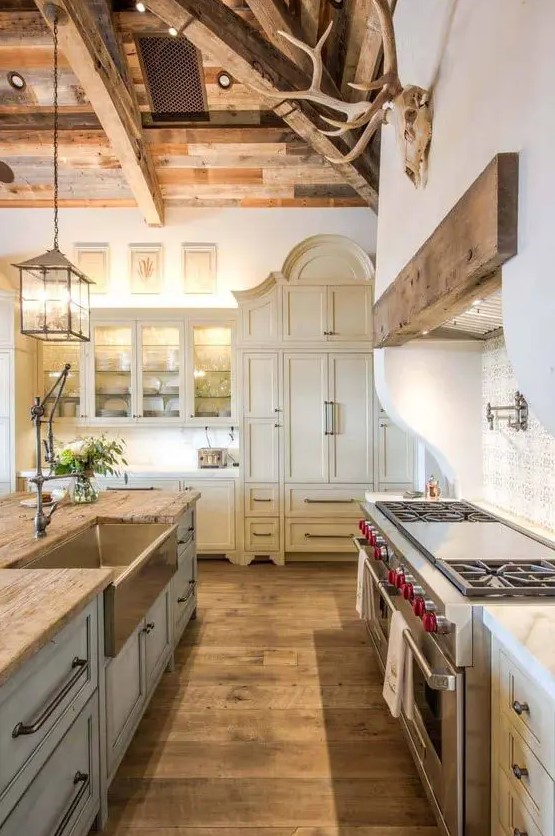 a sophisticated vintage barn kitchen with a beamed wood ceiling, cream Shaker-style cabinets, a light blue kitchen island, butcher block countertops and pendant lamps