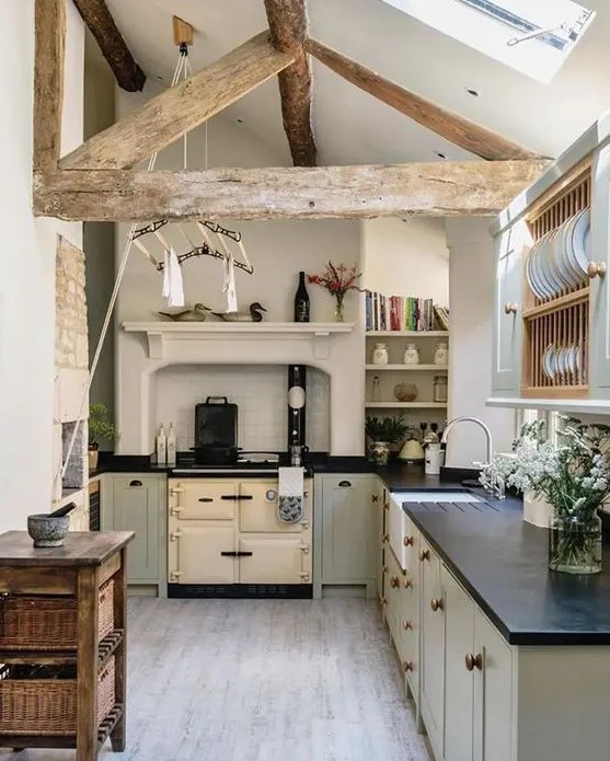 a small and cozy barn kitchen in neutral tones with a skylight, a reclaimed wood beam, dove gray kitchen cabinets with black countertops and a wooden kitchen island