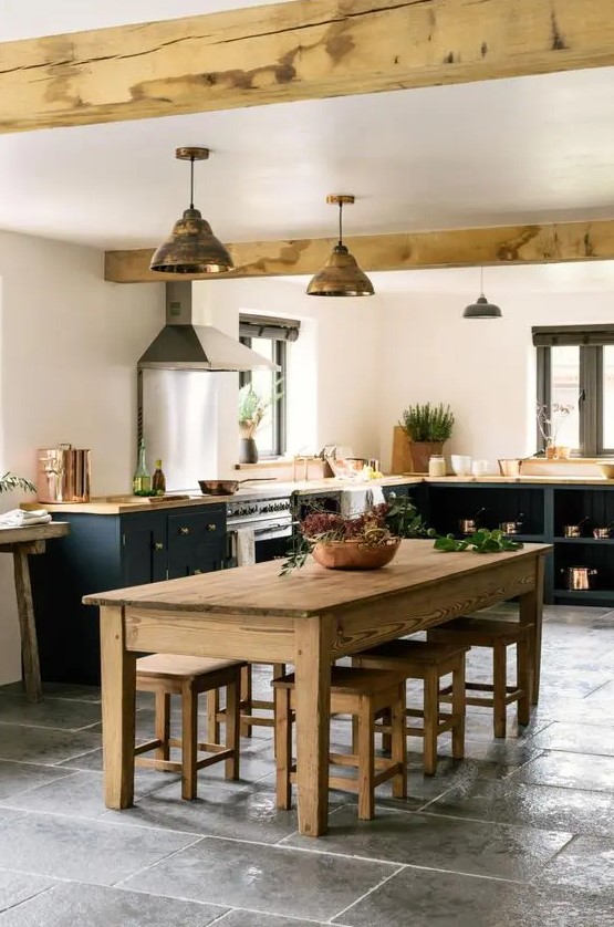 an inviting barn kitchen with black shaker-style cabinets and butcher block countertops, a stained dining set and exposed beams