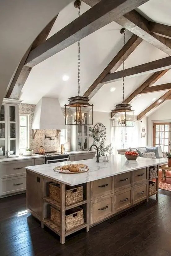an elegant barn kitchen with exposed beams, white shaker-style cabinets, a stained kitchen island, and vintage pendant lamps