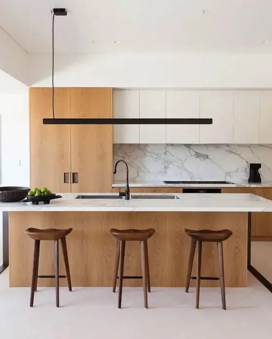 a chic modern kitchen with white and light stained cabinets, a large kitchen island with a white stone countertop and backsplash, a black pendant lamp