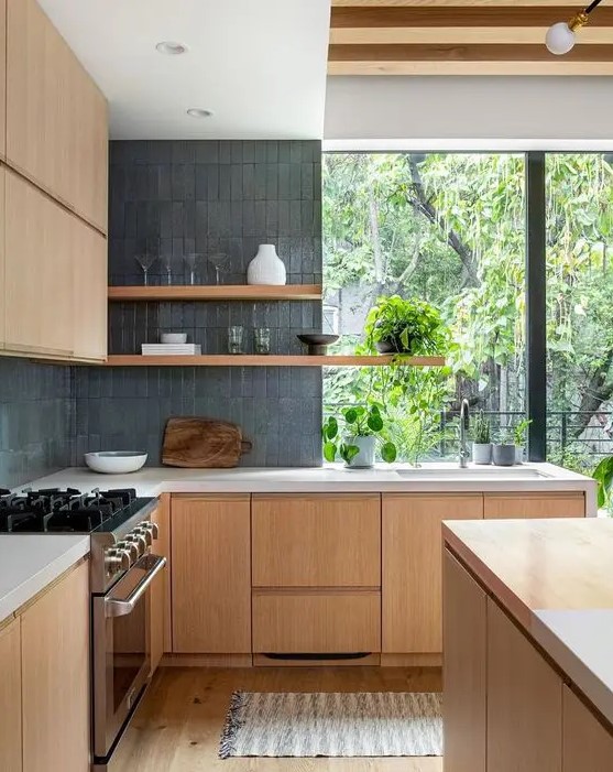 A beautiful, minimalist kitchen with stained cabinets, a gray thin-tiled backsplash, white stone countertops and long open shelves, plus a window with a view