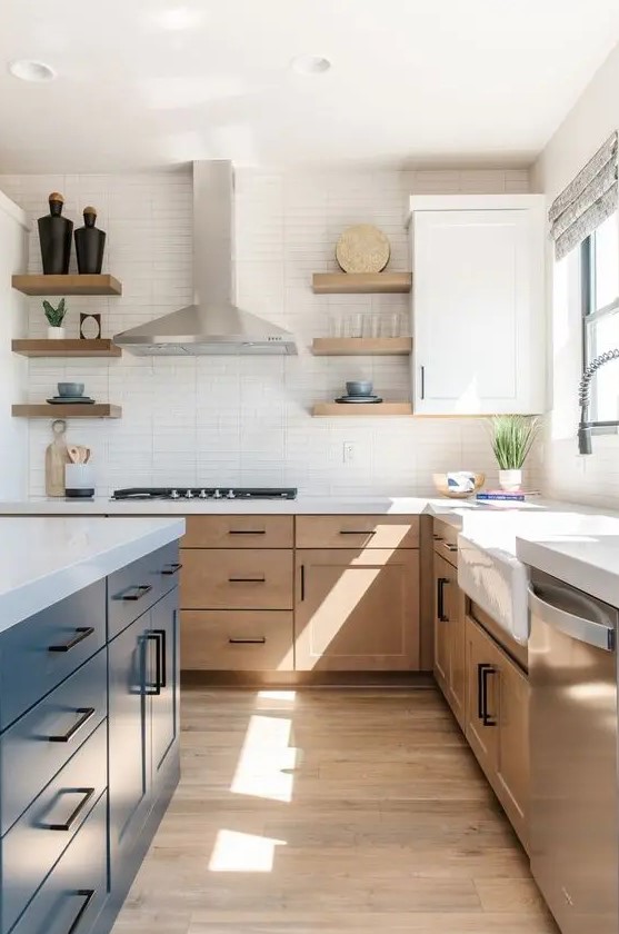a modern farmhouse kitchen with light stained cabinets, a navy island, white stone countertops and a narrow tile backsplash and black handles