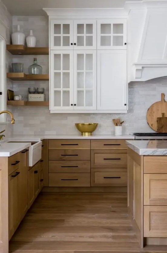 A modern farmhouse kitchen with white upper cabinets and stained lower cabinets, neutral tiles and corner shelves, and brass for a chic touch