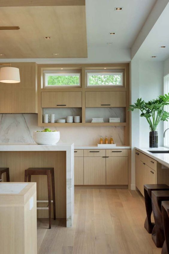 a modern, brightly stained kitchen with a white marble backsplash and worktops, simple lamps and windows here and there