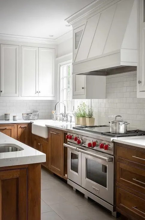 a rustic kitchen with white upper cabinets and stained lower cabinets, with white stone countertops and a white subway tile backsplash, a white extractor hood