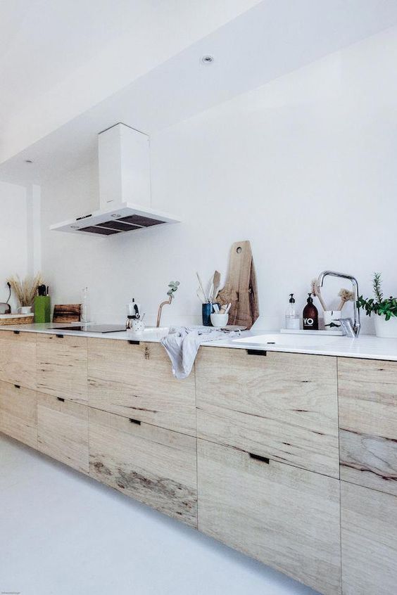 A Scandinavian kitchen with stained sleek cabinets, white stone countertops, a white hood, and metallic accents is cool
