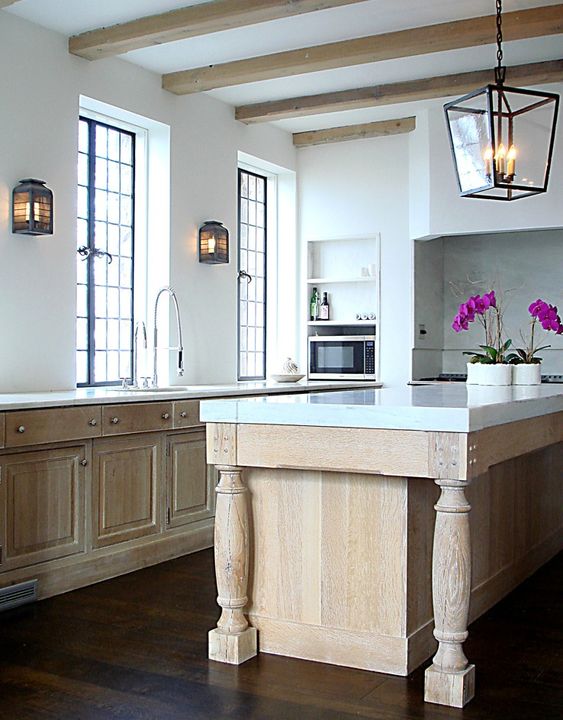 A vintage modern kitchen with stained cabinets, a large island and cabinet, white stone countertops and wooden beams