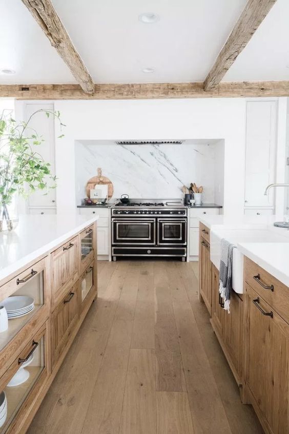 an inviting modern farmhouse kitchen with white and stained cabinets, white stone countertops, exposed beams and a black stove