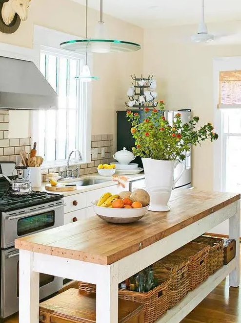 a cozy farmhouse kitchen with white cabinets, butcher block countertops, glass pendant lights, stainless steel appliances, and a tabletop kitchen island with open shelving and flowers
